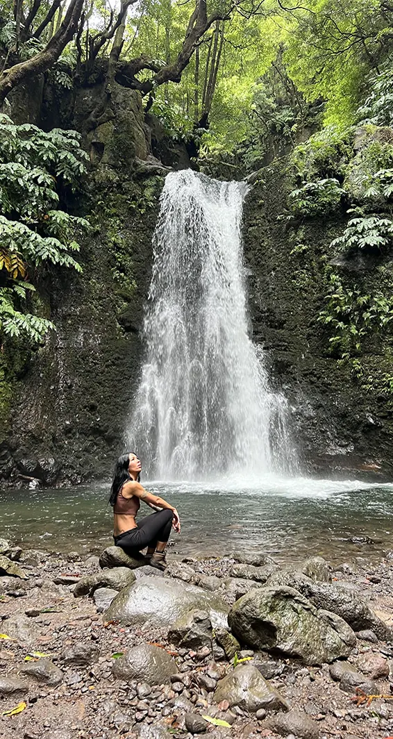 Francesca seduta su una roccia davanti a una cascata alle Azzorre, isola di São Miguel.